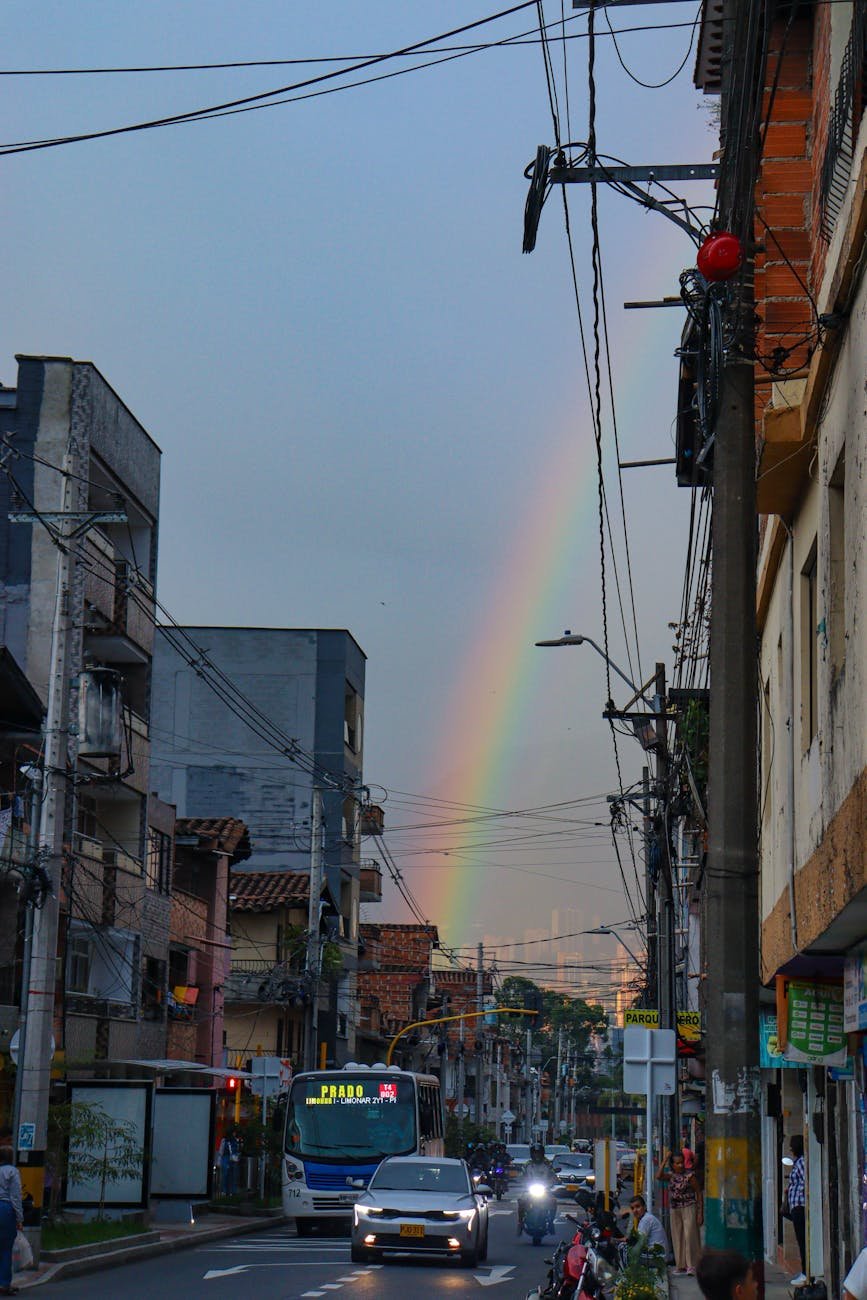 A colorful rainbow arches over a bustling street in Itagüi, capturing the essence of vibrant urban life in Colombia.